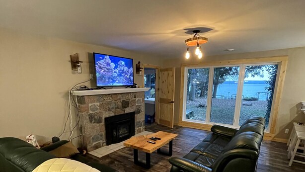 Una sala de estar con chimenea de piedra, televisor, sofá de cuero y un gran ventanal con vistas al exterior.