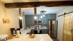 Una cocina moderna con una isla central, taburetes de bar, una lámpara colgante y una viga de techo de madera.