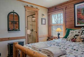 Un dormitorio acogedor con estructura de cama de madera, un ventanal con persianas, una lámpara de noche y un espejo montado en la pared.