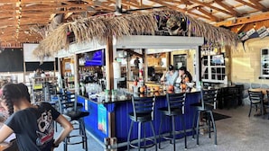 A tiki bar with a thatched roof, bar stools, and a counter with a bartender.