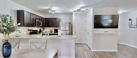 A modern kitchen with dark cabinets, a white countertop, and stainless steel appliances.