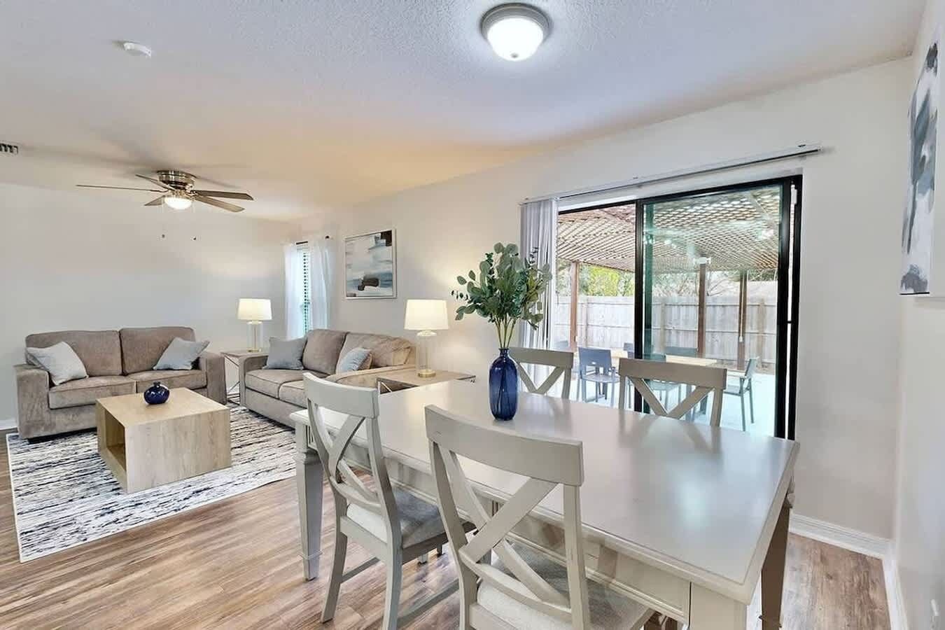 Ein modernes Wohnzimmer mit Essbereich, Deckenventilator und einer großen Schiebeglasdoor zu einer Außenpatio.