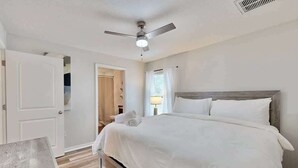 A bedroom with a bed, a ceiling fan, a nightstand, and a door leading to another room.
