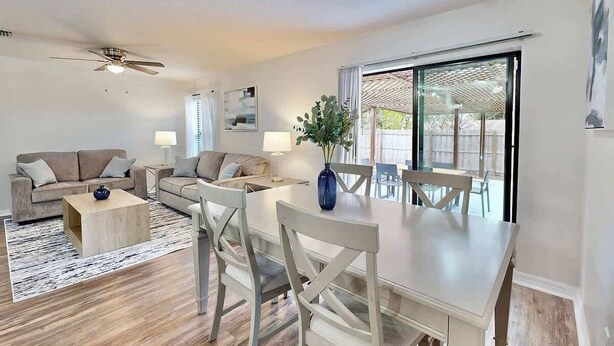 A spacious living room with a dining area, a ceiling fan, and a large sliding glass door leading to an outdoor patio.