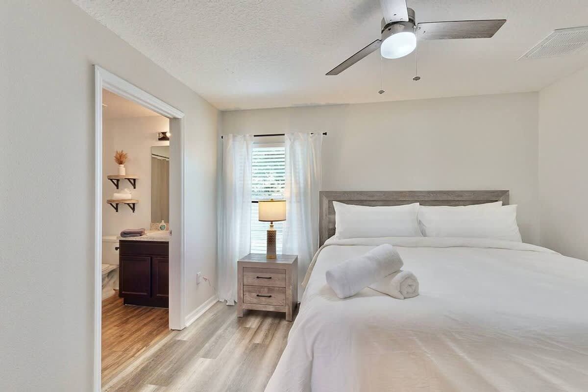 A hotel room with a bed, a nightstand, a ceiling fan, and a bathroom visible through an open door.