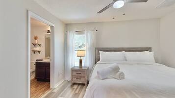A hotel room with a bed, a nightstand, a ceiling fan, and a bathroom visible through an open door.