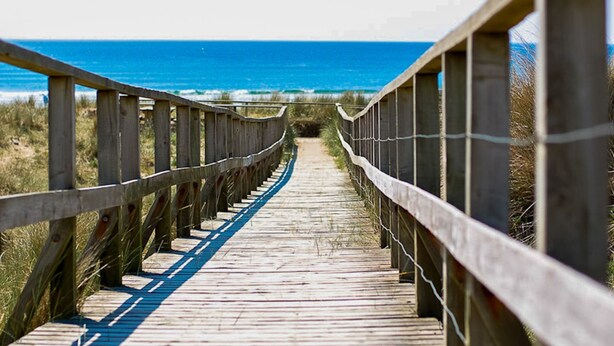 Una pasarela de madera que lleva a la playa, con vista despejada al océano.
