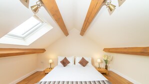 Un dormitorio con tragaluces, vigas de madera, una cama con almohadas, lámparas de noche y un tapete a rayas.