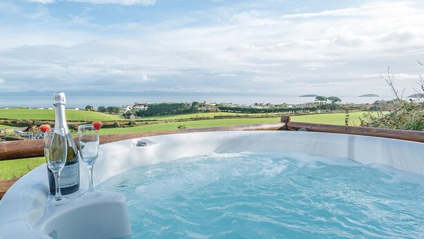 Un jacuzzi con una botella de vino rosado y copas, con vistas a un paisaje pintoresco con casas y vegetación.