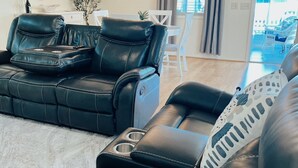 A modern living room with a black leather sofa, a dining table, and a chandelier. - 2 bdrm/2bath Patio Villa (The Villages)
