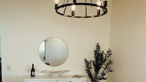 A dining area with a round table, white chairs, a chandelier, a mirror, a potted plant, and a white cabinet with glass doors. - 2 bdrm/2bath Patio Villa (The Villages)