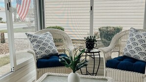 A sunroom with wicker furniture, a glass table, and a view of a house and flag. - 2 bdrm/2bath Patio Villa (The Villages)