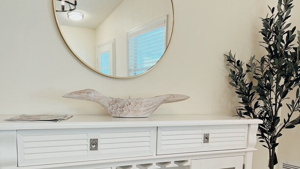A white wooden cabinet with a round mirror above it, a decorative bowl, and a potted plant beside it. - 2 bdrm/2bath Patio Villa (The Villages)