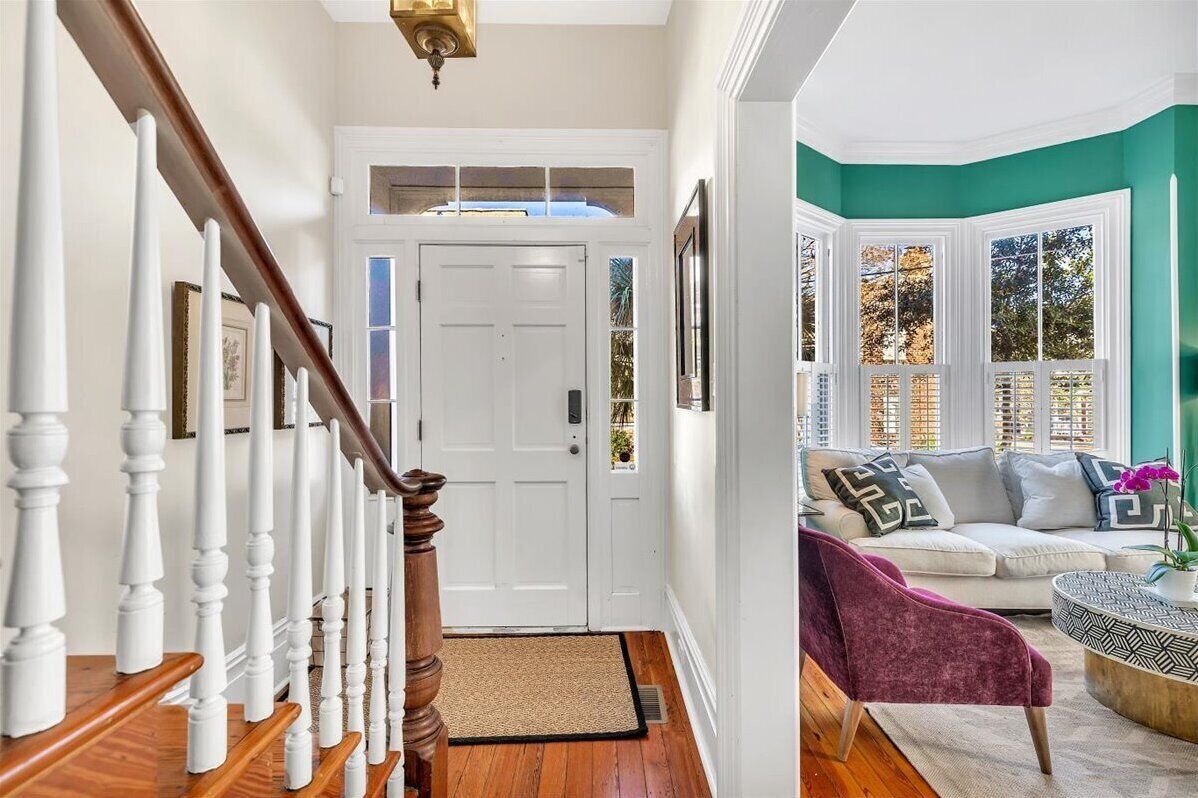 Un escalier avec des balustrades blanches, une porte blanche et une vue sur un salon avec un mur d’accent de couleur turquoise et un canapé blanc.