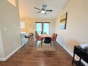 A dining area with a table set for four, a ceiling fan, and a view to the outside.