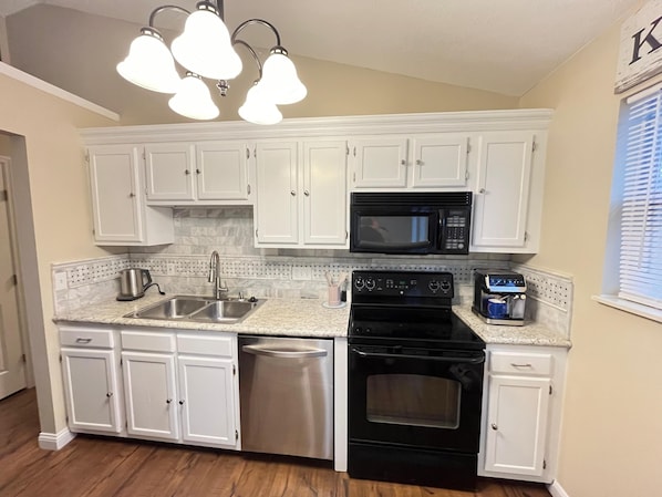 A kitchen with white cabinets, a stainless steel dishwasher, a black stove, and a microwave.
