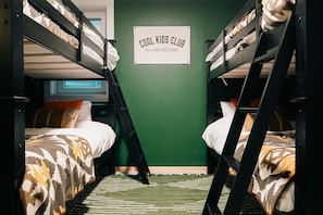 Habitación con literas y un cartel que dice 'COOL KIDS CLUB, TODOS SON BIENVENIDOS'.