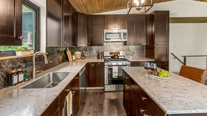 A modern kitchen with dark wood cabinets, stainless steel appliances, and a marble countertop. - NEW Hot Tub + Arcade + Fire Pit + Mtn Views (Bailey)