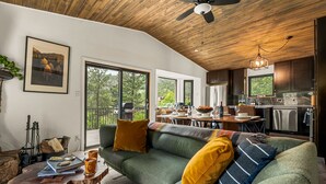 A modern living room with a green sofa, a wooden ceiling, and a view of the outdoors. - NEW Hot Tub + Arcade + Fire Pit + Mtn Views (Bailey)