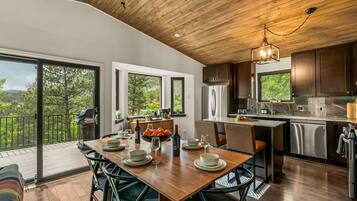 Une cuisine moderne avec un plafond en bois, de grandes fenêtres et un coin repas aménagé pour accueillir six personnes.