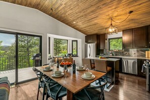 A modern kitchen with a wooden ceiling, large windows, and a dining area set for six. - NEW Hot Tub + Arcade + Fire Pit + Mtn Views (Bailey)