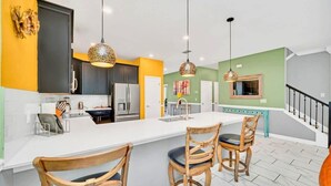 A modern kitchen with a central island, wooden chairs, pendant lighting, and a staircase leading to a dining area. - Endless Fun 9BR Sleeps 27, Pool+Spa@Championsgate (Davenport)