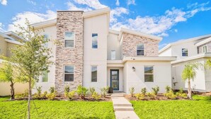 A modern two-story house with a stone facade, a front door, and a well-maintained lawn. - Endless Fun 9BR Sleeps 27, Pool+Spa@Championsgate (Davenport)