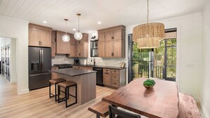 Una cocina moderna con armarios de madera, una isla central con taburetes y iluminación colgante, con vistas a zonas verdes al exterior.