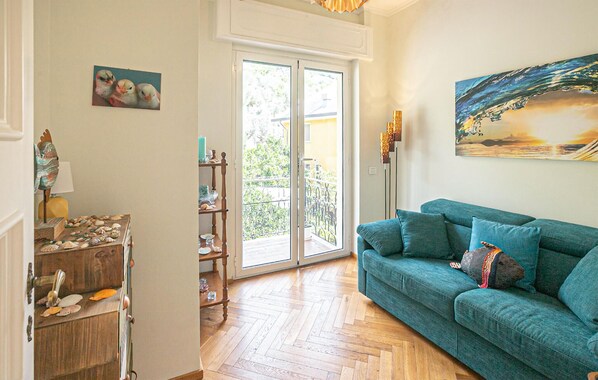 Un salon avec un canapé de couleur turquoise, un buffet en bois orné de coquillages, un tableau représentant un paysage marin et une porte-fenêtre coulissante donnant sur un balcon.