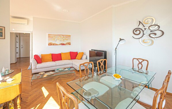 A modern living room with a glass dining table, wooden chairs, a sofa with colorful cushions, a flat-screen TV, and a decorative wall piece. - Stunning apartment in Bogliasco with WiFi (Bogliasco)