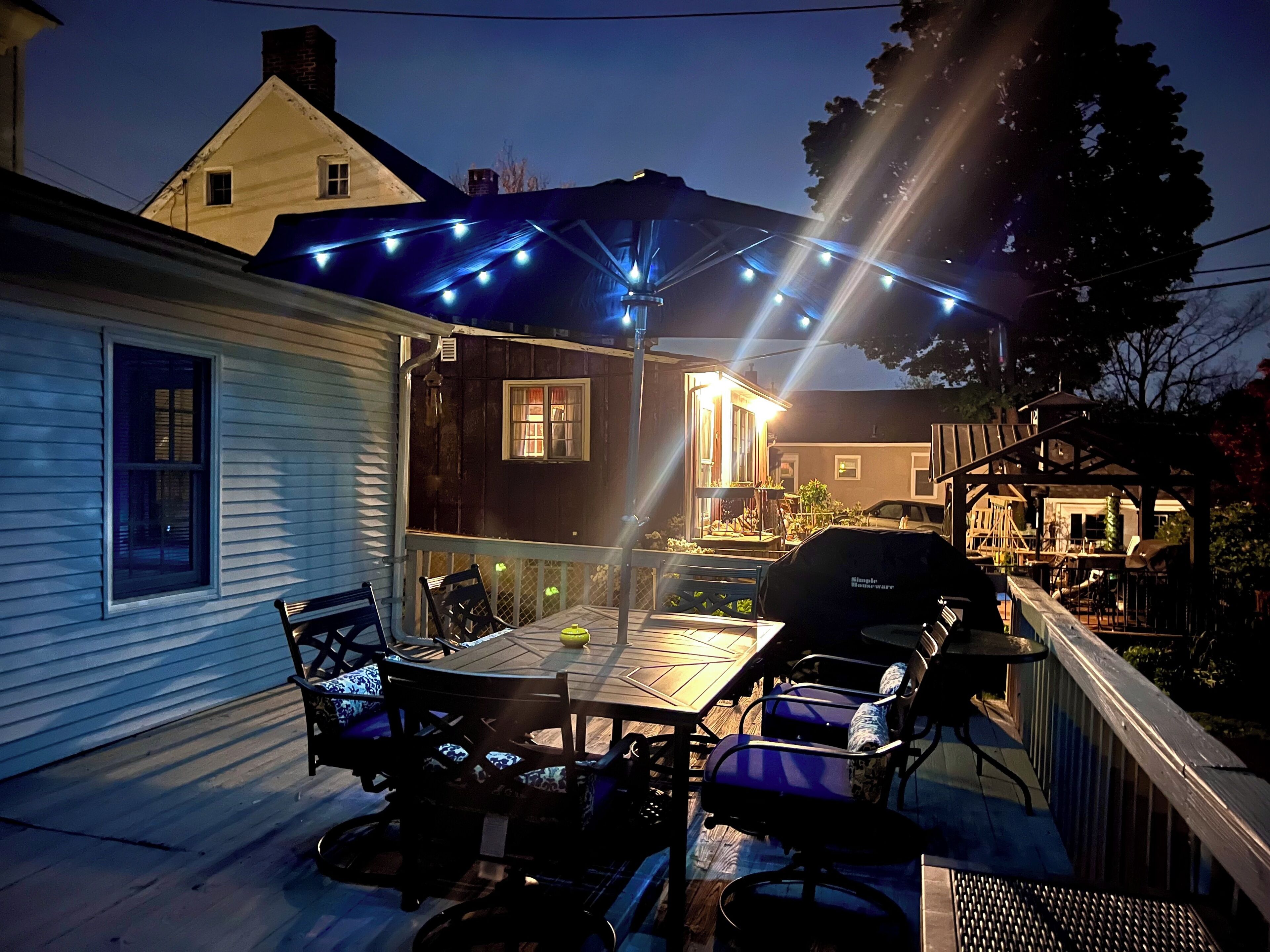 Une terrasse avec une table et des chaises, un barbecue et des guirlandes lumineuses.