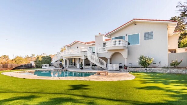 Uma casa grande de dois andares com piscina, varanda coberta e gramado bem cuidado.