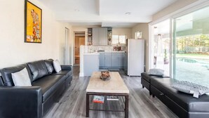 Sala de estar moderna com sofá de couro preto, mesa de centro de madeira e uma grande janela com vista para uma piscina.