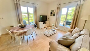 A living room with a sofa, a coffee table, a TV, and a dining table with chairs. - Splendide Appartement Dans Résidence Sécurisée Avec Piscine Proche du Village (La Croix-Valmer)