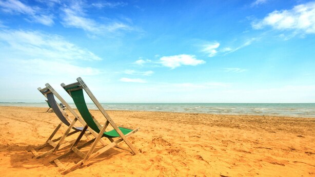 Une plage avec deux chaises de plage en bois et un coussin vert.