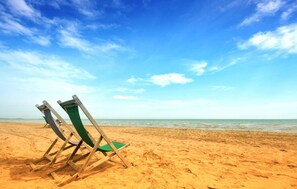 Una playa con dos sillas de madera y un cojín verde.