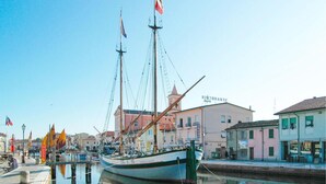 Un port où est amarré un grand voilier, des bâtiments avec des enseignes et une eau calme qui reflète le paysage.