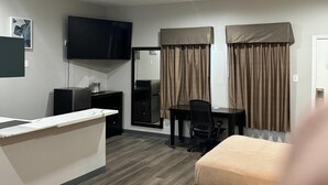 Ein Hotelzimmer mit Schreibtisch, Stuhl, Bett, Fernseher und Vorhängen.