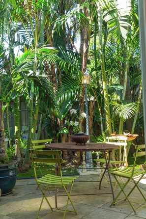 Een terras buiten met een tafel en stoelen, omgeven door weelderig groen en een decoratieve lantaarnpaal.