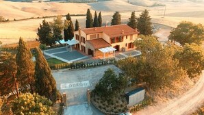 Una casa de dos pisos con techo de tejas, rodeada de árboles y un paisaje montañoso.