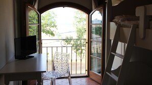 Una habitación con televisión sobre una mesa, una silla, una escalera y vistas a través de un amplio ventanal de arco.