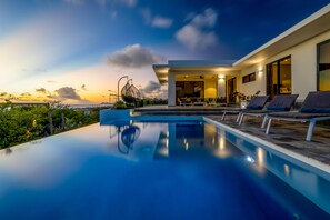 A modern poolside area with lounge chairs, a dining area, and a view of the sunset. - Beautiful villa with infinity pool and gorgeous ocean view. Perfect for divers! (Kralendijk)