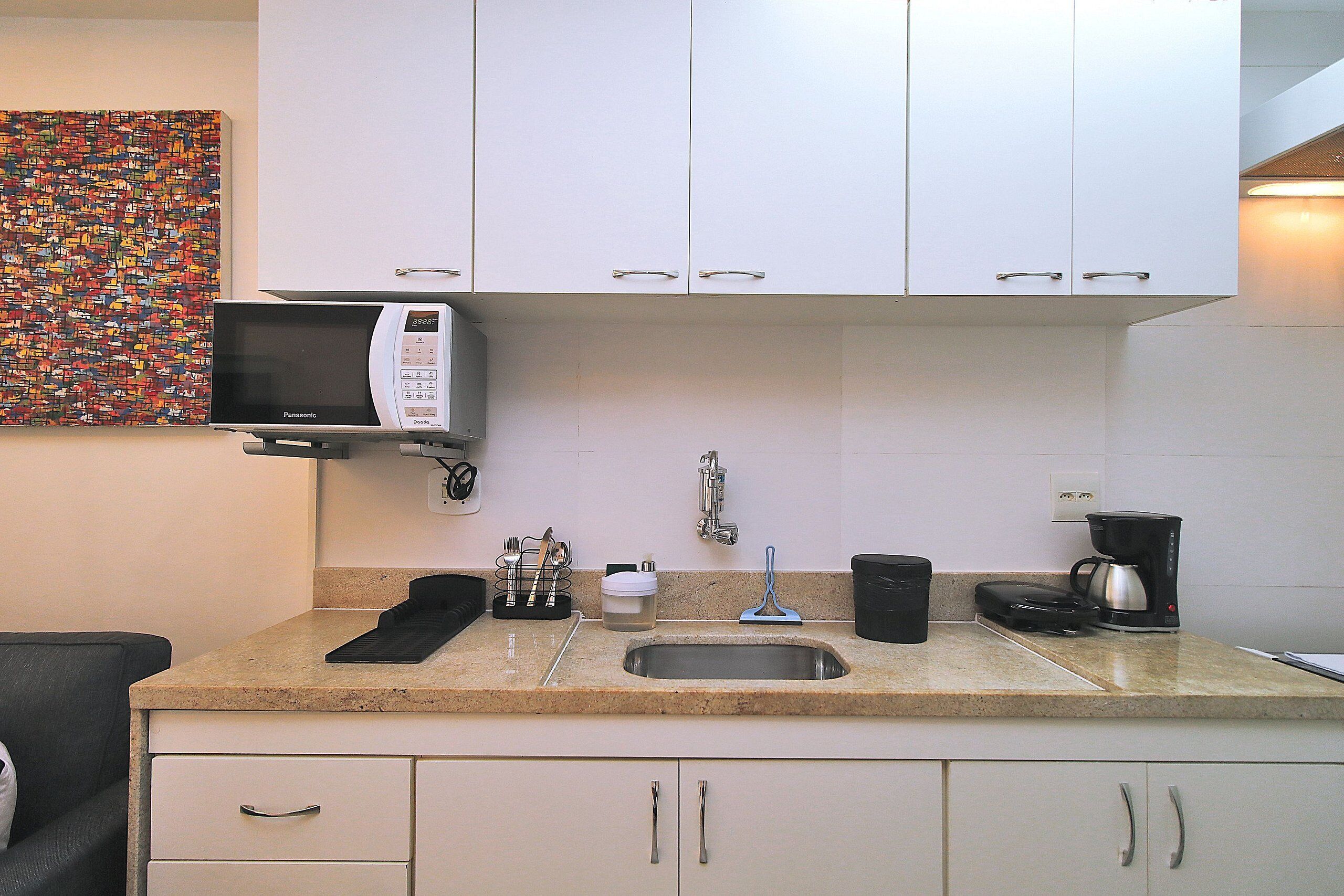 Una kitchenette con microondas, cafetera y lavamanos.