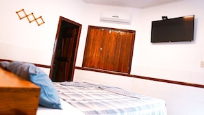 A bedroom with a bed, wooden wardrobe, and a flat-screen TV mounted on the wall. - Pousada Costa Azul (Maraú)
