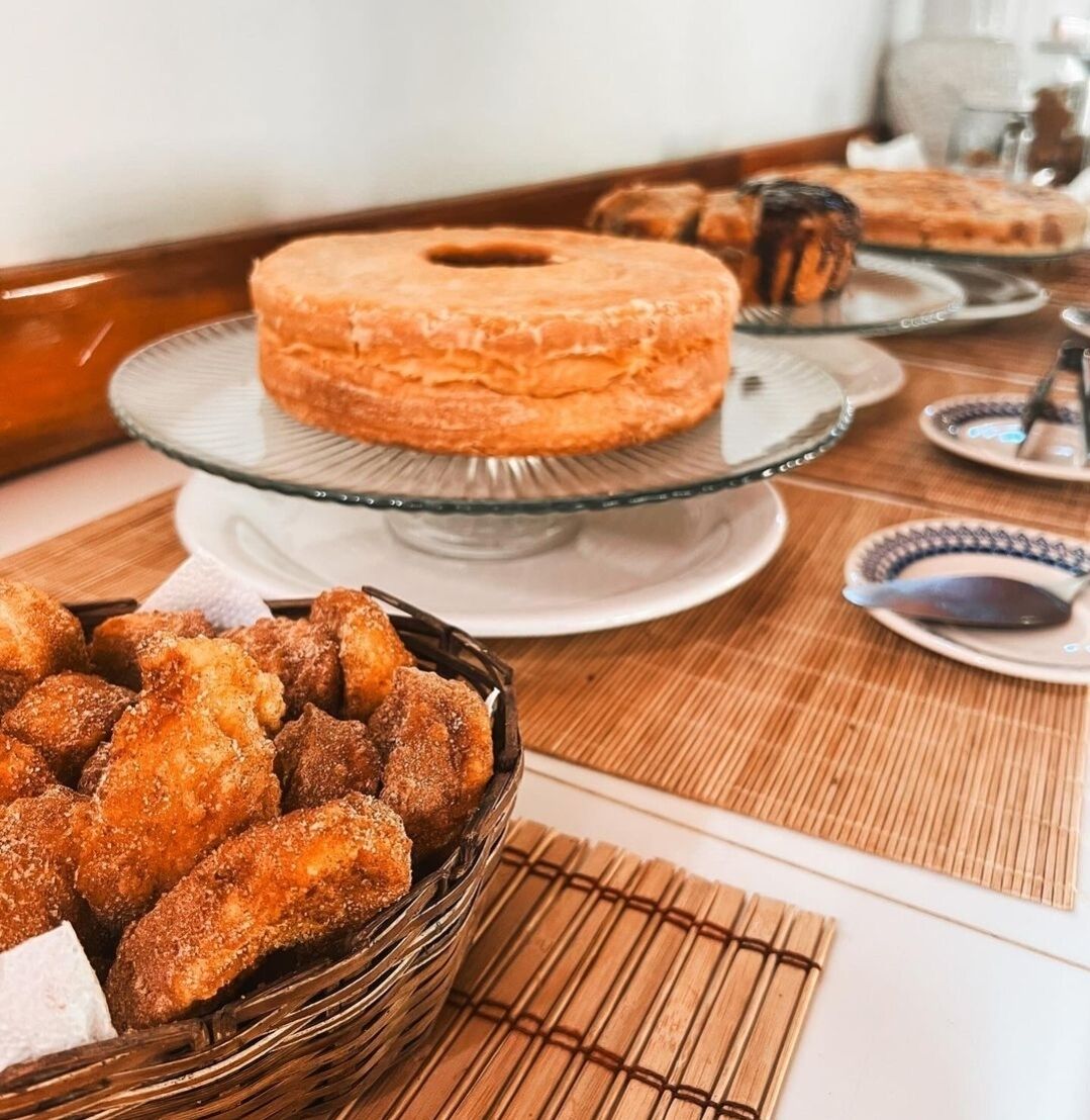 Un tavolo da buffet con diversi cibi, tra cui un donut glassato di grandi dimensioni su un piedistallo di vetro, un cestino di alette di pollo impanate e diverse pirofile con salse.
