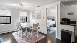 Une cuisine moderne dotée d’une cuisinière intégrée, un coin repas avec une table et des chaises, et une chambre à coucher avec un lit et une table de chevet.