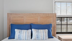 Un lit avec une tête de lit en bois, deux oreillers bleus et un oreiller blanc à rayures.