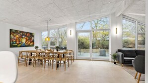 En rummelig stue med et stort spisebord, stole, en sofa og et maleri på væggen.