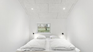 Et minimalistisk soveværelse med en seng, et vindue med udsigt til træer og et loft med indbygningsbelysning.