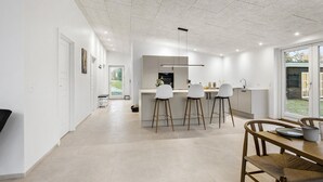 Et moderne køkken med en central ø, barstole og et spiseområde med et træbord og stole.